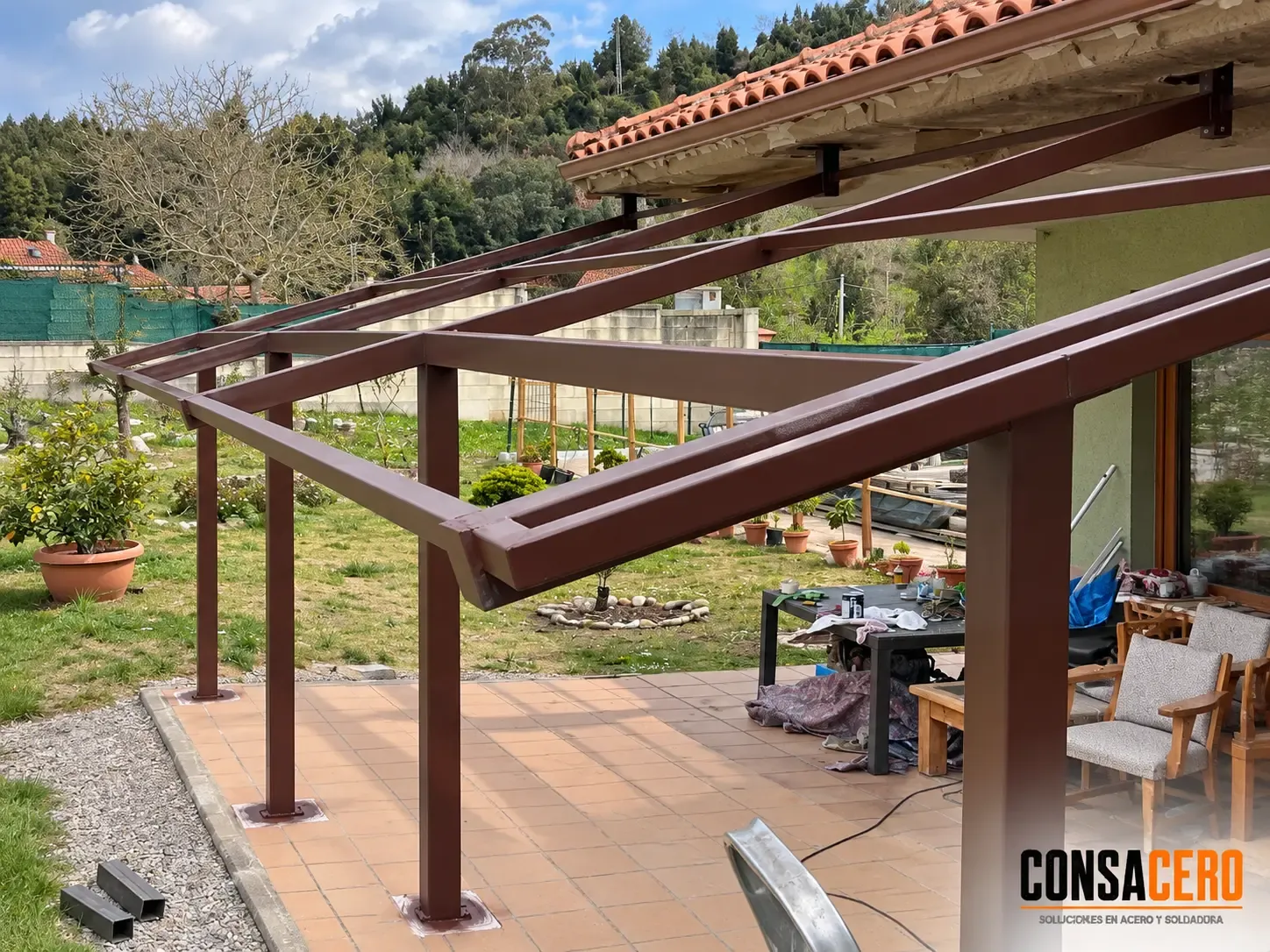 Estructura de pérgola de acero en montaje junto a una vivienda